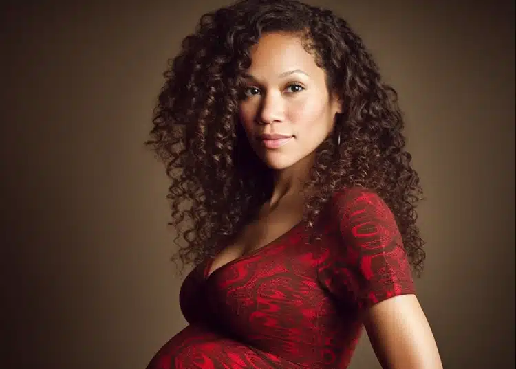 A glowing mom to be with dark curly hair is wearing a red dress and is absolutely stunning.